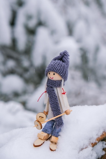 Angel gnome in scarf and knitted hat skiing on snowy fir branch Elf toy on skis in snowy landscape