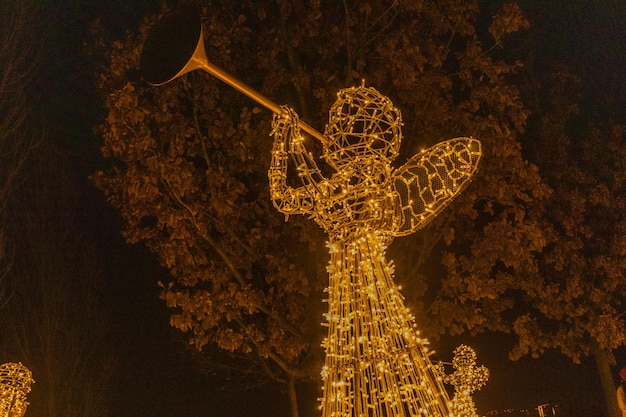 Angel with a lantern made of garlands of lights in a city park