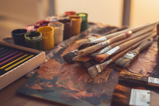 Angle view photo of palette with mixed oil paints gouache crayons and paintbrushes set in art studio