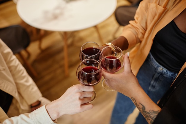 Above angle of young multicultural friends clinking with glasses of red wine while standing in front