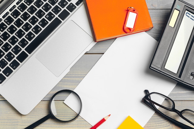 Angled View of laptop Computer Keyboard and glasses with Various Office Supplies on wooden Desk