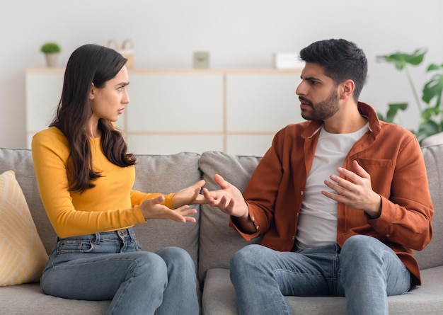 Angry arabic spouses having quarrel arguing sitting on couch indoor