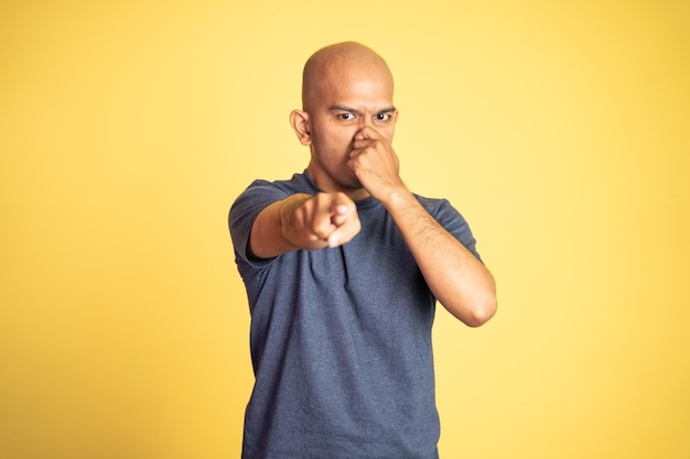 Angry asian bald man covering nose with finger pointing