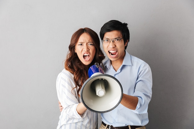 Angry asian business couple standing isolated, holding loudspeaker