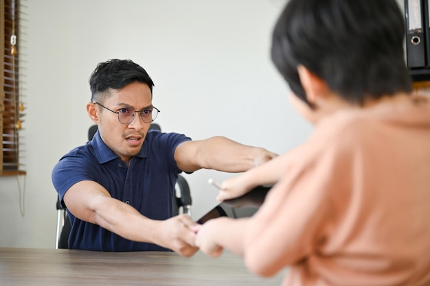 Angry Asian dad taking out a tablet from his son having tablet battle fight