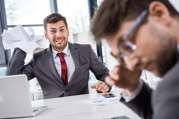 Angry boss throwing papers at upset colleague at business meeting