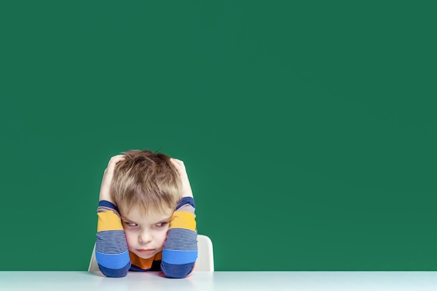 An angry boy sits at a desk holding his head Copy space