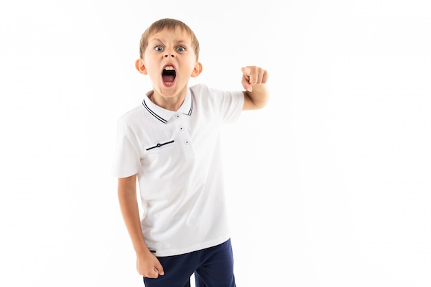 Angry boy with bangs in a white t-shirt on white wall with copy space