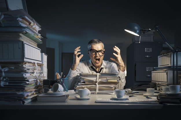 Angry businessman overloaded by paperwork