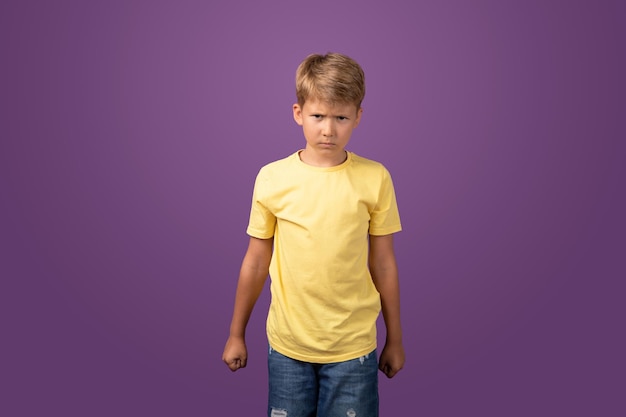 Angry Caucasian preteen boy clenching fists and looking at camera with aggressive face expression while standing on purple background Studio shot