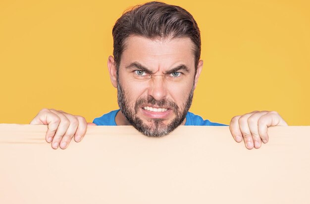 Photo angry close up face of man with blank banner ad posing isolated over studio background portrait of attractive man holding empty blank poster man showing blank poster male presenting signboard