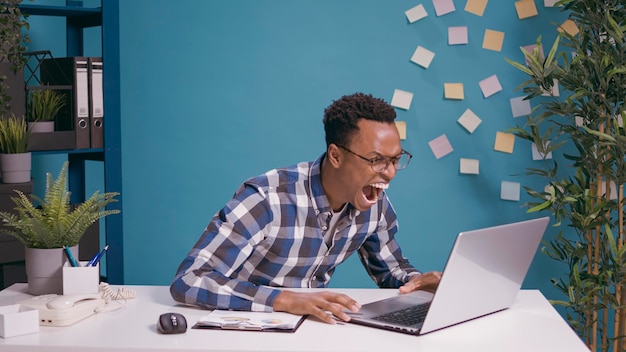 Angry employee shouting at laptop screen feeling frustrated about work mistake. Irritated furious person screaming and yelling at computer, having problem with network at desk. Business failure