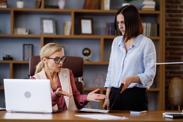 Angry female boss scolding sad and scared office worker Demanding manager leader is annoyed at laziness and mistakes in paperwork of employee Authoritarian leadership abuse of power