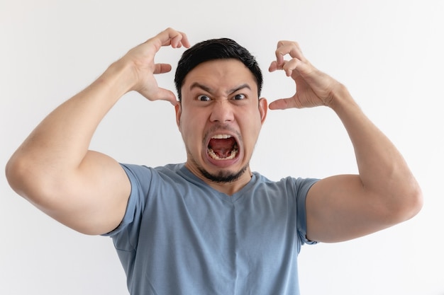 Angry and mad face of Asian man in blue t-shirt on isolated background.