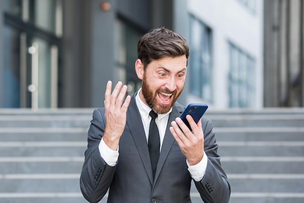 Angry male businessman cry talking on the phone outside business man shouting on call outdoors. Nervous mad professional conversation on smartphone. Irritated employee scream speak at urban street