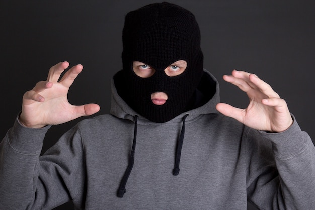 Angry man criminal in black mask over grey background