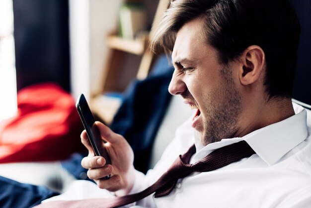 Angry man in suit screaming at smartphone after party