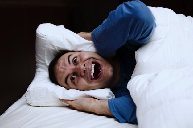 Angry man using a pillow to cover his ears