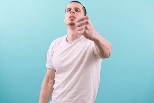 An angry man in a white tshirt shows his fist on a blue backgroundNegative Power Rage Relationship Standing Strength Stressed Strong Tough Violence Aggressive Mad Arm Evil