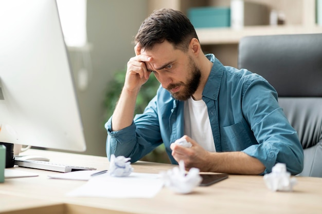 Angry stressed businessman crumpling paper while sitting at desk in office