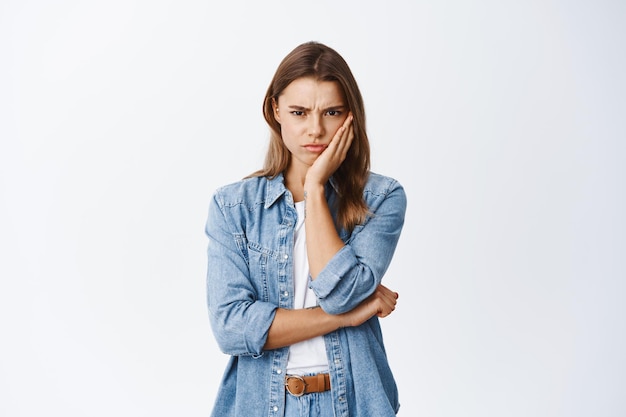 Angry and upset blond girl frowning, looking with dismay and hate, sulking and staring something unfair and disappointing, standing on white