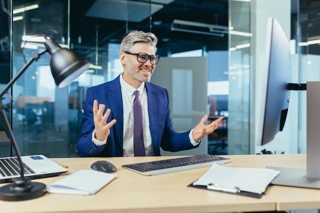 Angry and upset boss businessman shouting at computer monitor man with glasses working in modern office at computer