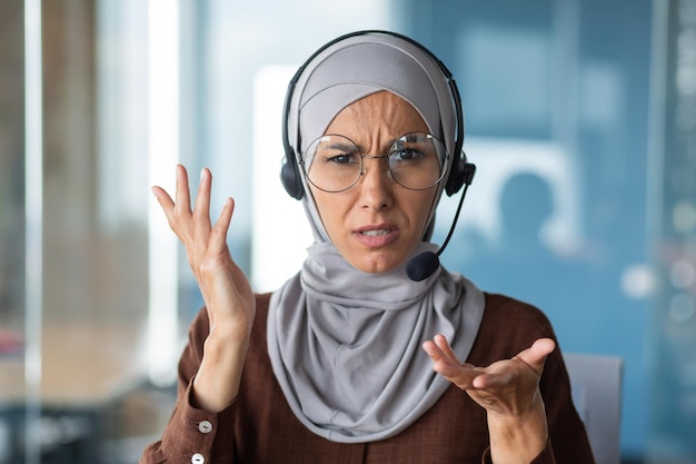 Angry woman in hijab talking on video call businesswoman with headset phone closeup looking at web