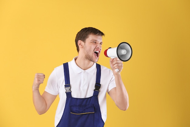 Angry worker shouting into megaphone on color background