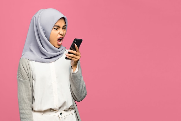 Angry young Asian woman holding mobile phone with mouth opened