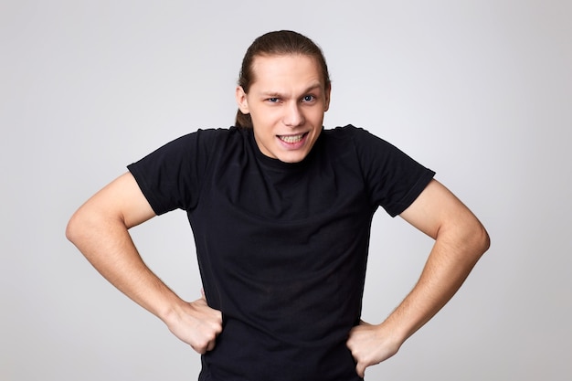 Angry young man in black t-shirt isolated on gray background