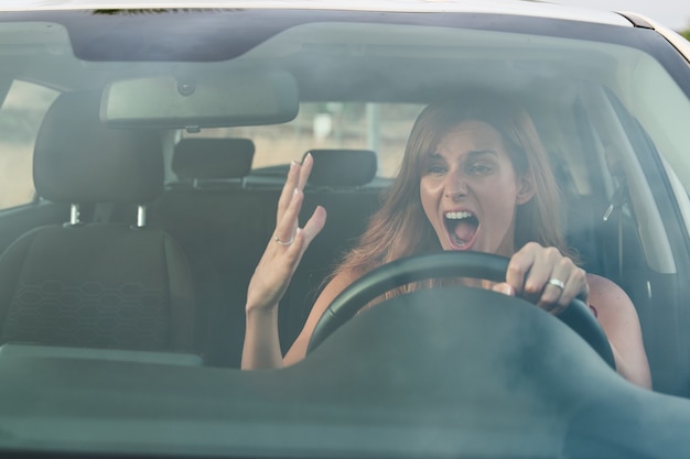 Angry young pretty woman inside her car while driving. Road safety concept