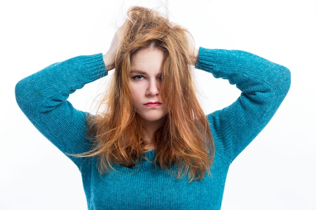 An angry young redhaired girl with tousled hair is holding her head Negative emotions and migraine White background