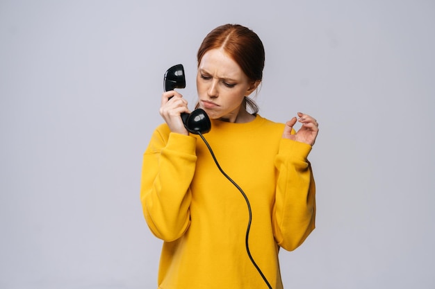 Angry young woman in stylish sweater holding handset receiver of retro phone and looking on him