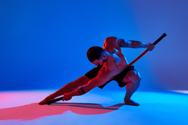 Animal instinct fitness instructor sportsman showing his incredible flexibility with an animal flow move in studio against a pink blue gradient background