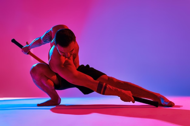 Animal instinct fitness instructor sportsman showing his incredible flexibility with an animal flow move in studio against a pink blue gradient background