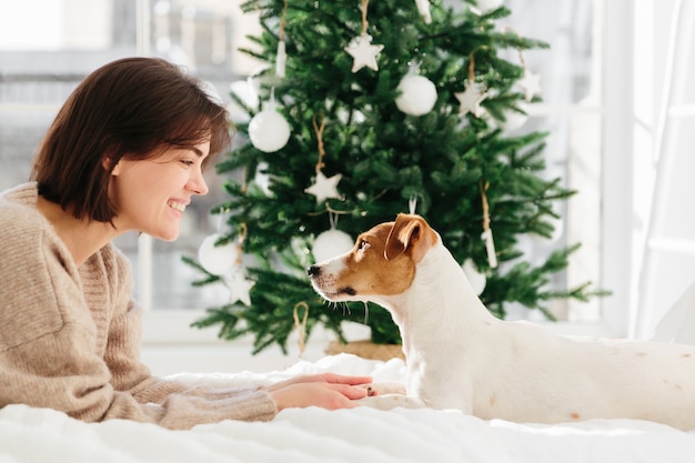 Animals, loyalty and people . Smiling brunette lady in oversized brown sweater plays with pedigree dog