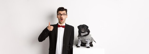 Animals party and celebration concept handsome young man in suit and cute black pug in costume stari