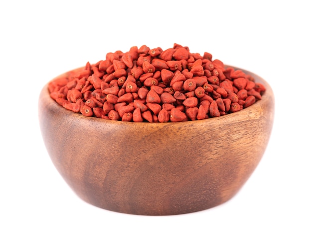 Annatto seeds in wooden bowl, isolated on white.