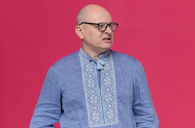 Annoyed adult slavic man in blue shirt wearing optical glasses looking at side