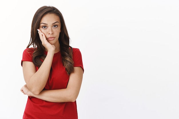 Annoyed bothered intense young brunette woman in red t-shirt, furrow eyebrows, lean face palm, stare camera indifferent and bored, express disdain and lack of interest, not care at all