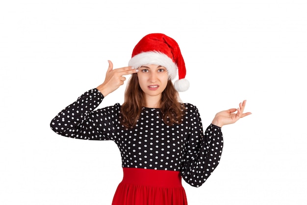 Annoyed and displeased woman in dress shrugging and holding fingers on temple. emotional girl in santa claus christmas hat isolated on white . holiday 