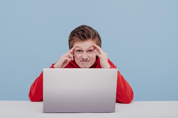 Annoyed preteen child boy getting nervous during computer game look in camera on blue background