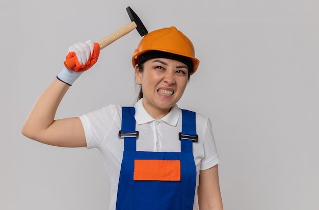 Annoyed young asian builder girl with orange safety helmet and safety gloves holding hammer 