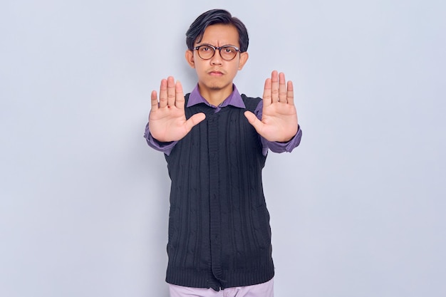 Annoyed young Asian man in casual shirt makes stop gesture saying no isolated on white background