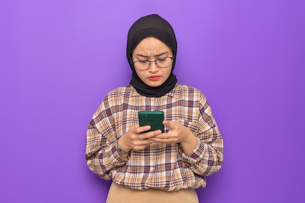 Annoyed young Asian woman in plaid shirt using mobile phone received bad news isolated on purple background