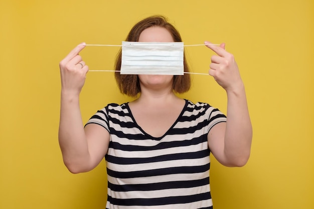 Anonym caucasian woman shows in hands medical mask on a yellow background