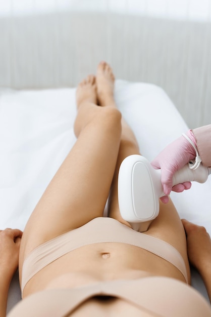 Anonymous beautician in gloves using laser hair removal apparatus on bikini zone of female client