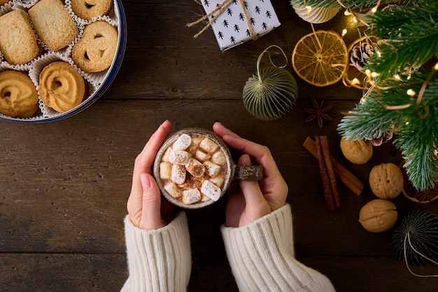 Anonymous female in white sweater holding cup of hot cocoa with marshmallows and grated chocolate