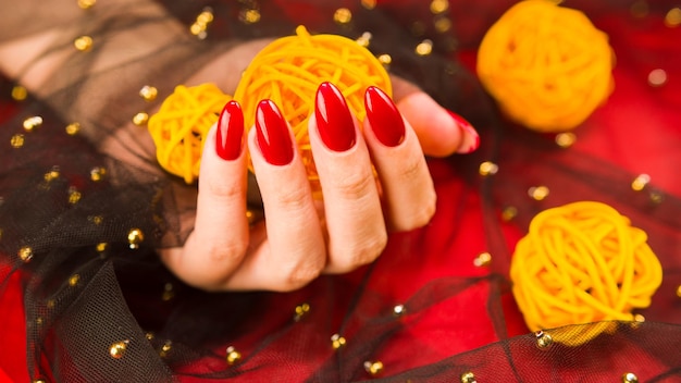 Anonymous female with red manicure with decorative wicker balls on red background