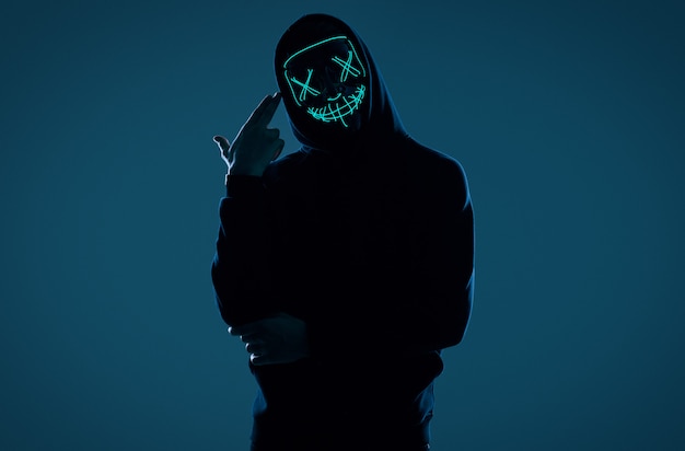 Photo anonymous man in black hoodie hiding his face behind a neon mask